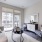 Spacious and well lit living room with wood floors and a large window with access to the kitchen